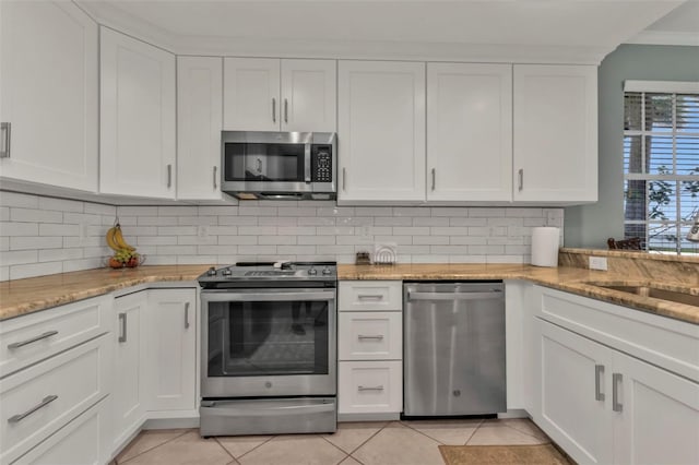 kitchen featuring crown molding, decorative backsplash, appliances with stainless steel finishes, white cabinets, and light tile patterned flooring