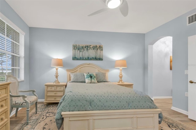 bedroom with baseboards, visible vents, a ceiling fan, arched walkways, and wood finished floors