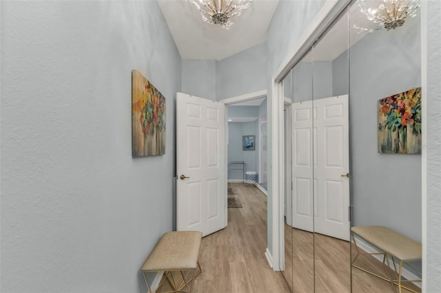 hall with baseboards, light wood-type flooring, and a notable chandelier