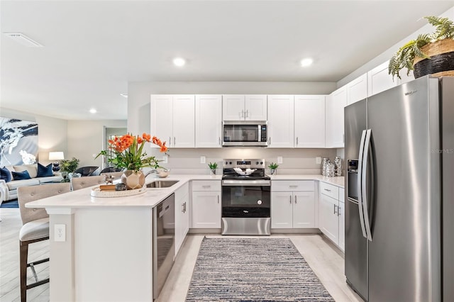 kitchen with stainless steel appliances, white cabinets, open floor plan, light countertops, and a kitchen breakfast bar