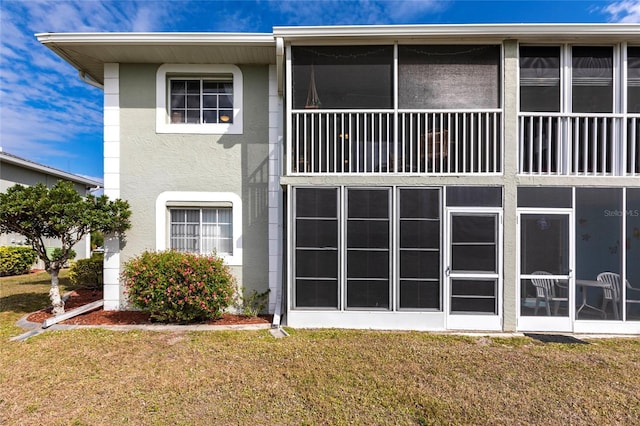 back of property with a yard, a sunroom, and stucco siding