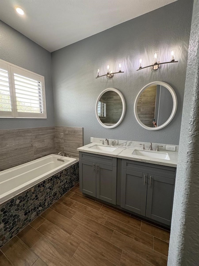 bathroom featuring a garden tub, a textured wall, a sink, and wood tiled floor