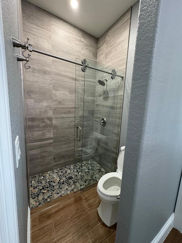 bathroom featuring toilet, a stall shower, and wood finished floors