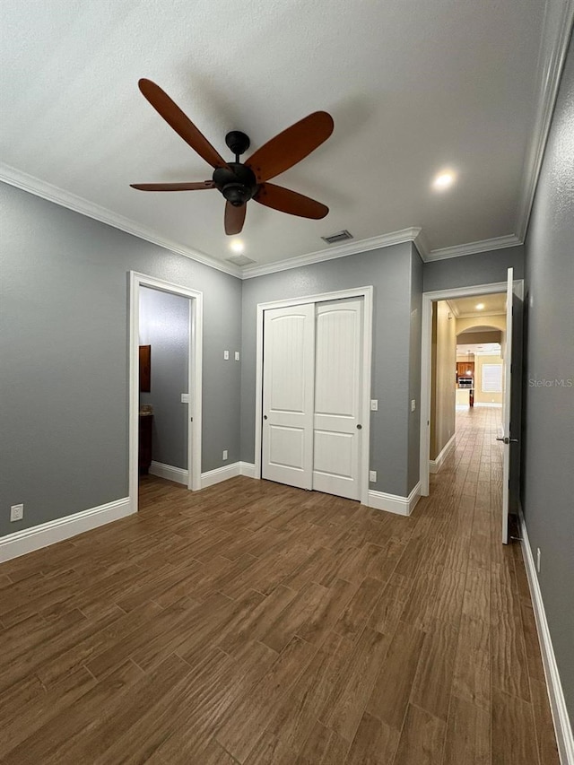 unfurnished bedroom featuring arched walkways, dark wood-type flooring, visible vents, baseboards, and crown molding