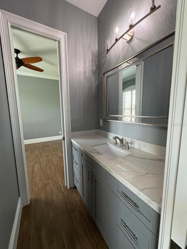 bathroom featuring wood finished floors, vanity, baseboards, a ceiling fan, and ornamental molding