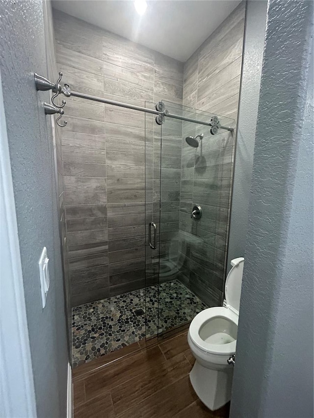 bathroom with a stall shower, a textured wall, toilet, and wood finished floors