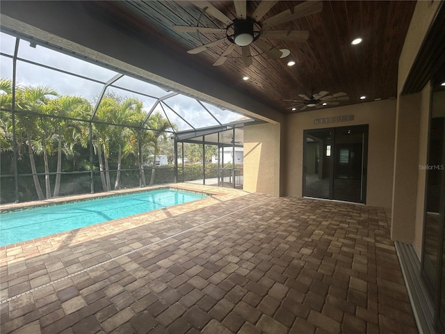 outdoor pool featuring glass enclosure, a patio area, and a ceiling fan