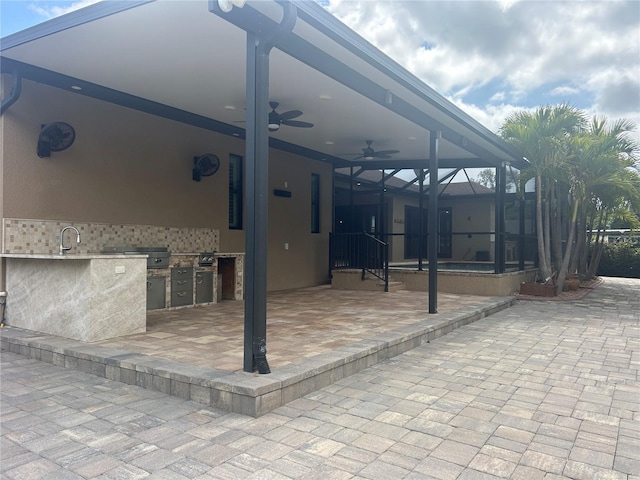 view of patio featuring a sink, glass enclosure, ceiling fan, and exterior kitchen