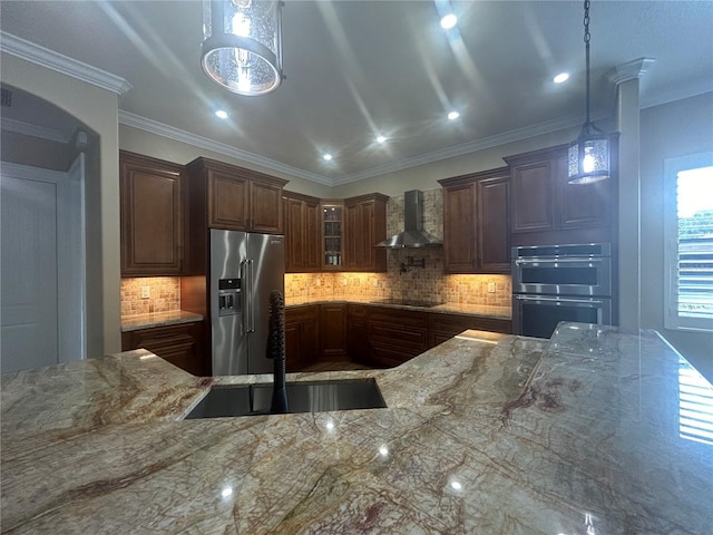 kitchen featuring light stone counters, a sink, hanging light fixtures, appliances with stainless steel finishes, and wall chimney range hood