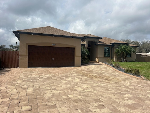 view of front of home featuring roof with shingles, an attached garage, fence, decorative driveway, and stucco siding