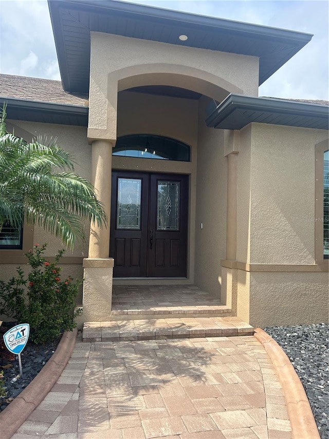 entrance to property with french doors, roof with shingles, and stucco siding