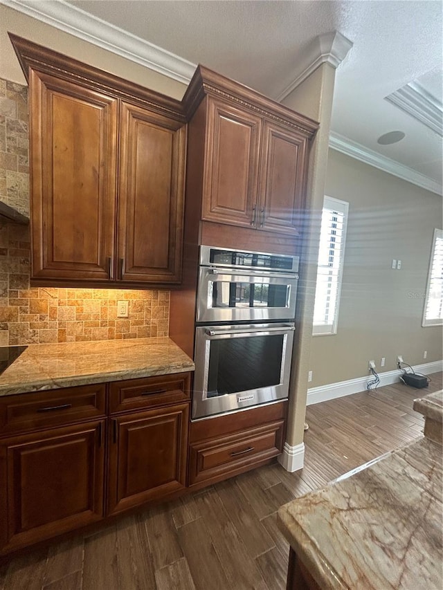 kitchen with dark wood finished floors, decorative backsplash, ornamental molding, light stone countertops, and stainless steel double oven