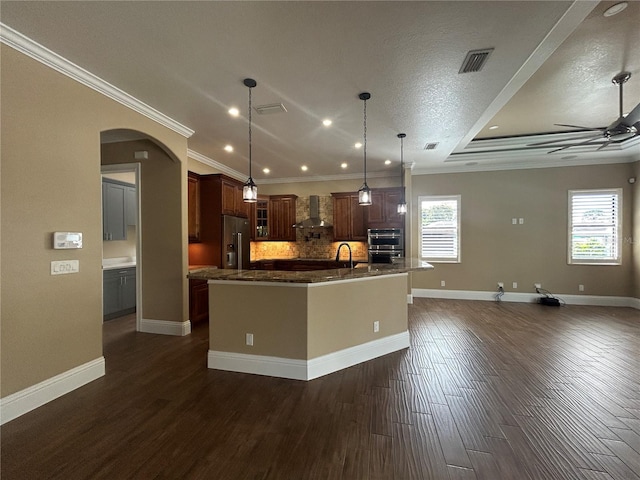 kitchen with visible vents, hanging light fixtures, glass insert cabinets, wall chimney range hood, and an island with sink