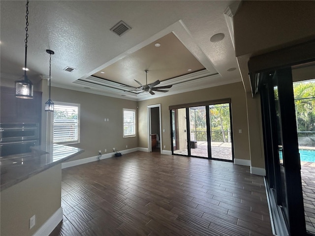 unfurnished living room with a tray ceiling, plenty of natural light, dark wood finished floors, and visible vents