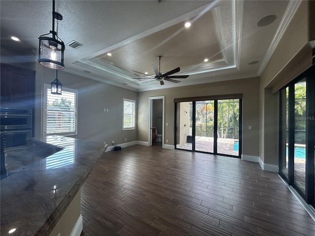 unfurnished living room with baseboards, a raised ceiling, ceiling fan, dark wood-style flooring, and crown molding