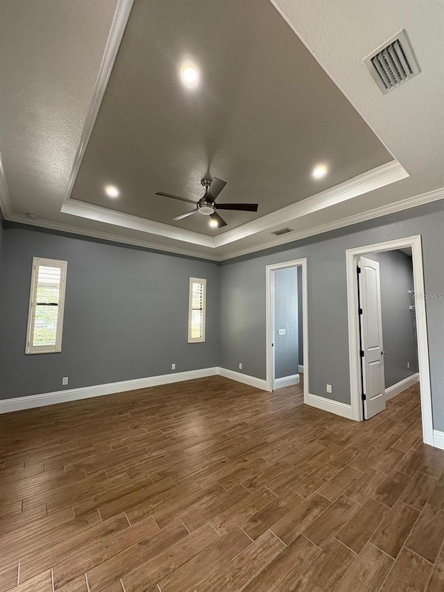 empty room with a wealth of natural light, a tray ceiling, visible vents, and dark wood finished floors