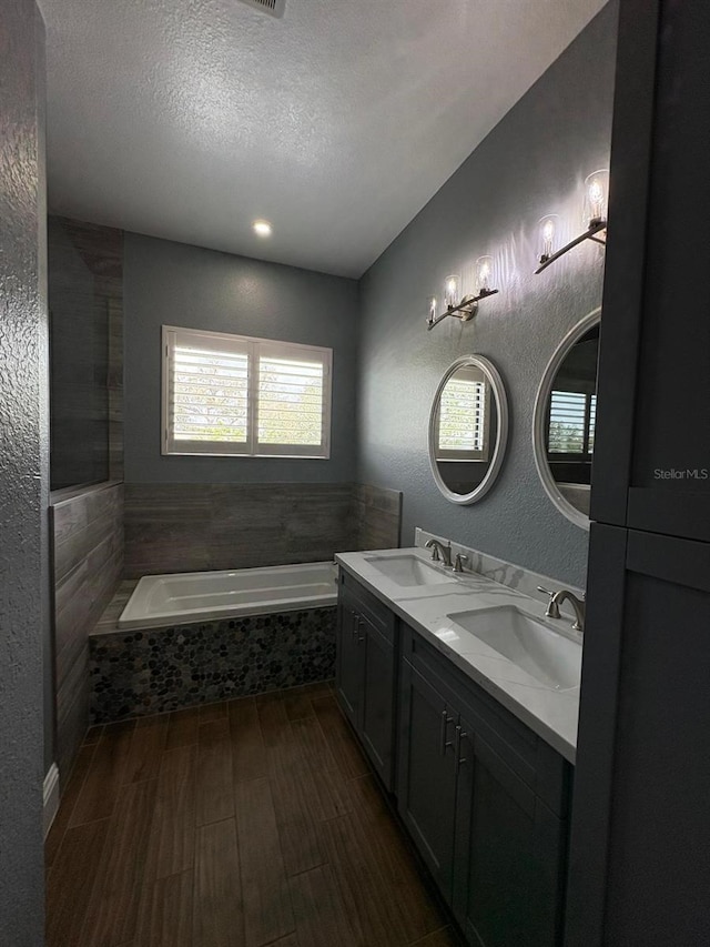 bathroom featuring a garden tub, a textured wall, a textured ceiling, and a sink