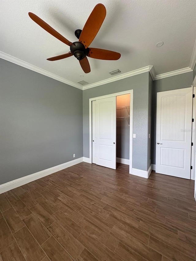 unfurnished bedroom featuring dark wood-style floors, baseboards, visible vents, and crown molding