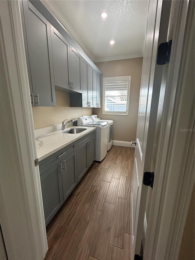 laundry area featuring cabinet space, ornamental molding, wood tiled floor, a sink, and washer and dryer