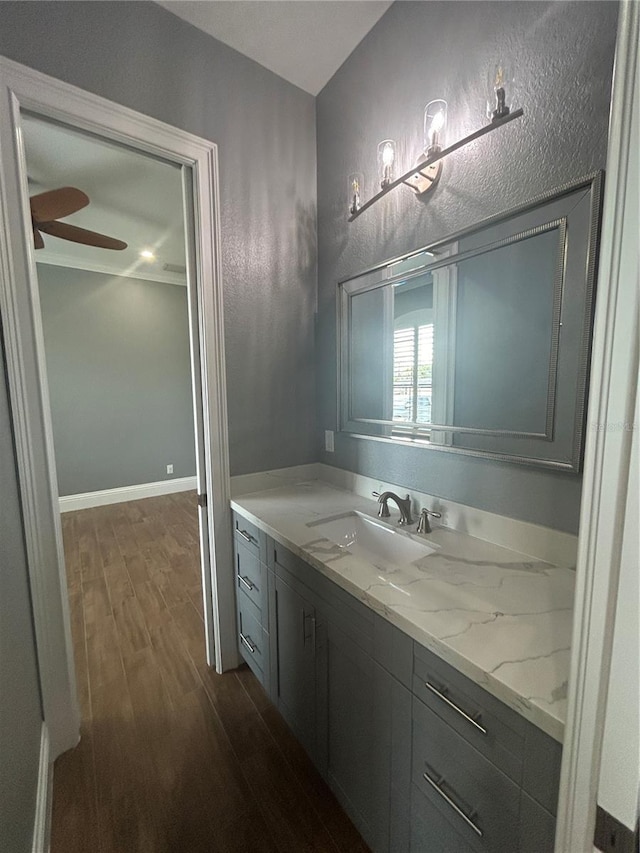 bathroom featuring a textured wall, a ceiling fan, vanity, wood finished floors, and baseboards