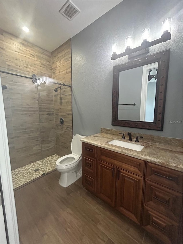 full bath featuring toilet, wood finished floors, vanity, visible vents, and a shower stall