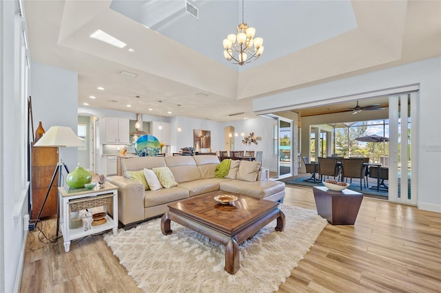 living room featuring light wood finished floors, visible vents, arched walkways, a tray ceiling, and a chandelier