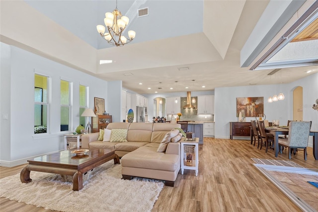 living area featuring baseboards, visible vents, arched walkways, an inviting chandelier, and light wood-type flooring