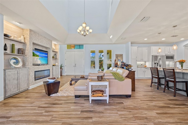 living area featuring a chandelier, light wood-type flooring, a fireplace, and visible vents