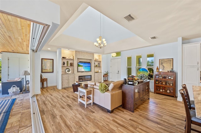 living room with visible vents, an inviting chandelier, light wood-type flooring, built in shelves, and a fireplace