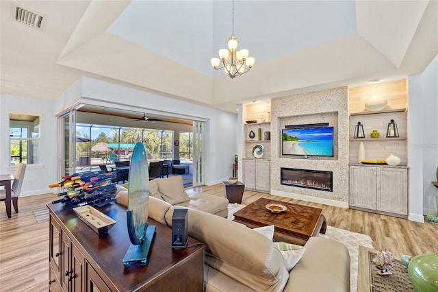 living room featuring visible vents, built in features, light wood-style flooring, an inviting chandelier, and a fireplace