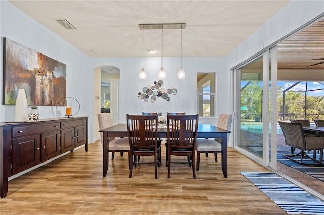 dining space with arched walkways, visible vents, and light wood finished floors