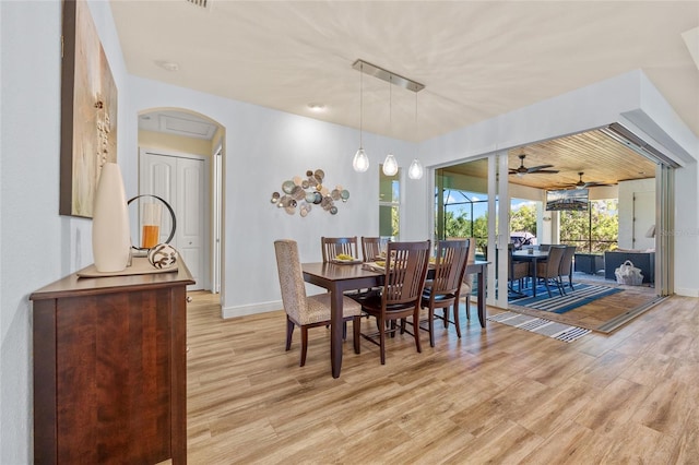 dining area featuring arched walkways, light wood finished floors, and baseboards