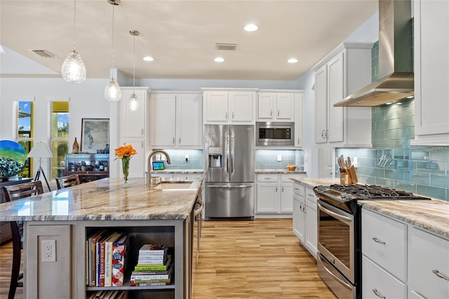 kitchen with stainless steel appliances, visible vents, a sink, wall chimney range hood, and a kitchen breakfast bar