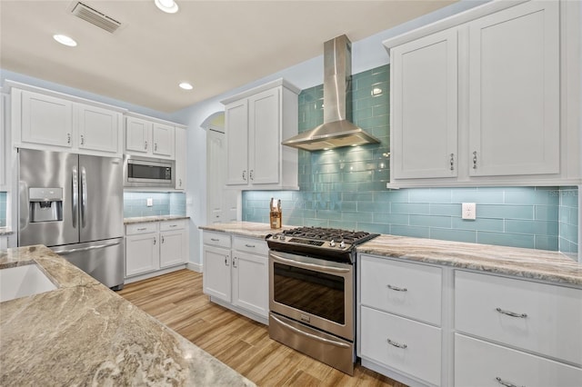 kitchen featuring light wood finished floors, visible vents, appliances with stainless steel finishes, white cabinetry, and wall chimney range hood