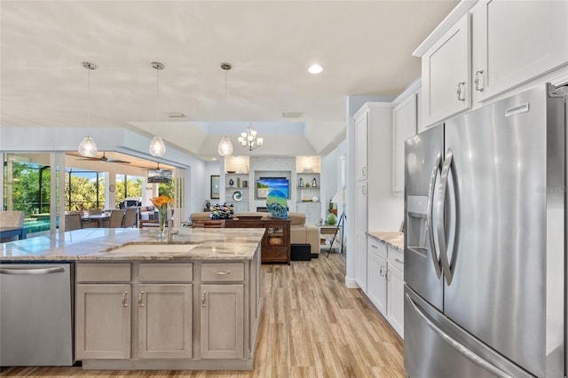 kitchen with light wood-style flooring, appliances with stainless steel finishes, open floor plan, light stone counters, and white cabinetry