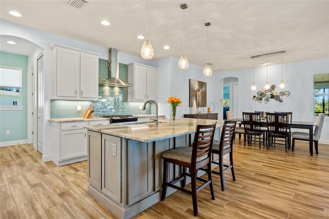 kitchen featuring arched walkways, backsplash, light wood-style floors, a sink, and wall chimney exhaust hood