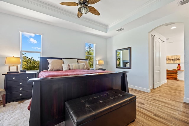 bedroom featuring arched walkways, a tray ceiling, visible vents, ornamental molding, and light wood-style floors