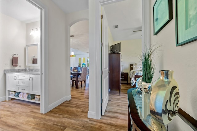 corridor featuring arched walkways, baseboards, visible vents, and light wood-style floors