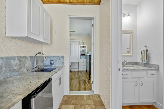 kitchen featuring light stone counters, white cabinetry, dishwasher, and a sink