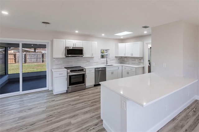 kitchen with stainless steel appliances, a sink, visible vents, white cabinetry, and backsplash