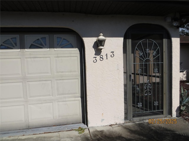 entrance to property with a garage and stucco siding