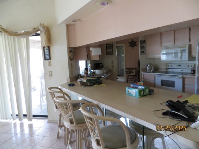 kitchen with white appliances, a breakfast bar, light countertops, and light tile patterned flooring