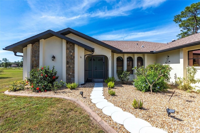 view of front of property with a shingled roof, a front yard, stone siding, and stucco siding