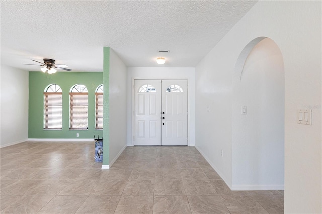 entrance foyer featuring arched walkways, ceiling fan, a textured ceiling, and baseboards