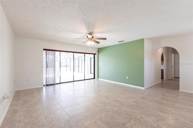 unfurnished room with arched walkways, visible vents, a ceiling fan, a textured ceiling, and baseboards