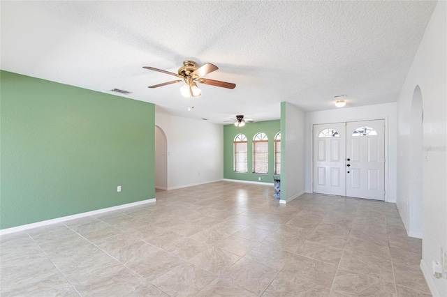 entryway with arched walkways, a textured ceiling, a ceiling fan, visible vents, and baseboards