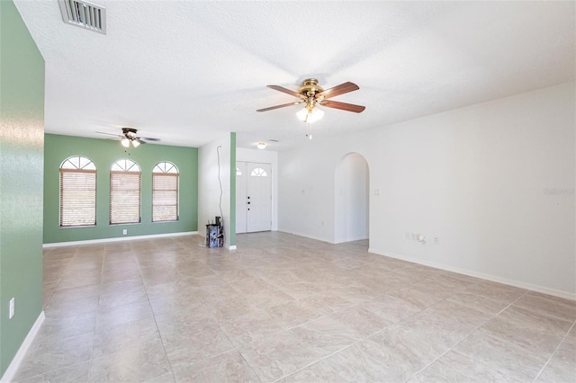 unfurnished room featuring arched walkways, a textured ceiling, visible vents, baseboards, and a ceiling fan