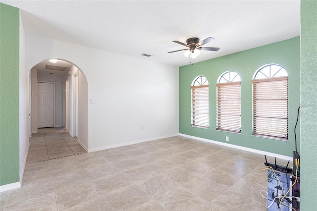 unfurnished room featuring baseboards, visible vents, arched walkways, and a ceiling fan