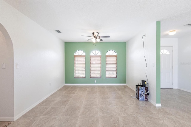 empty room featuring baseboards, visible vents, arched walkways, ceiling fan, and a textured ceiling