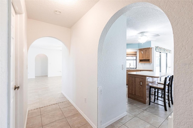 hallway with a sink, light tile patterned floors, arched walkways, and a textured ceiling